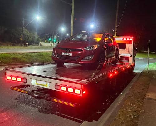 A tow truck is towing a car late at night in an emergency.