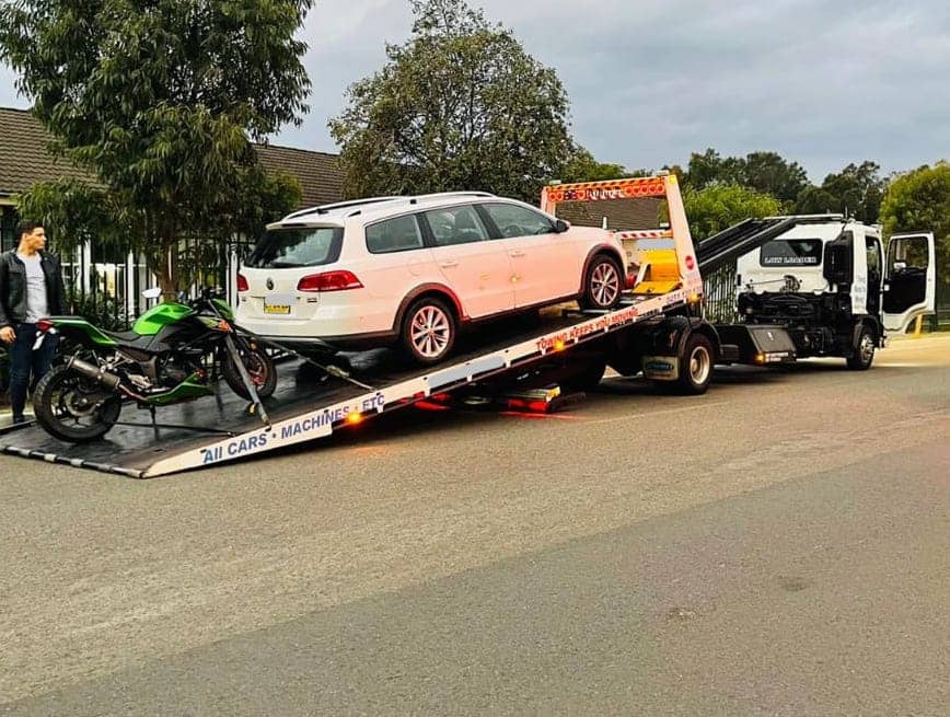 A tilt tray truck towing a car and a bike.