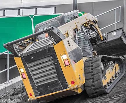 A bobcat driving up a steep hill on a job site.