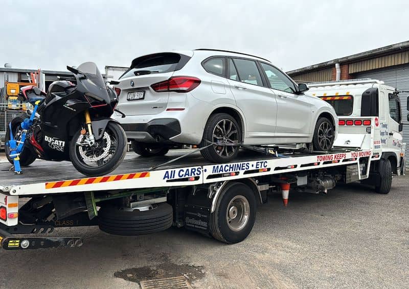 A car and a motorbike on the back of a tilt tray truck.