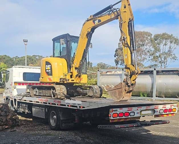 A medium sized excavator being transported by a tow truck.