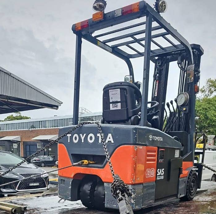 A forklift chained down on a tow truck bed.