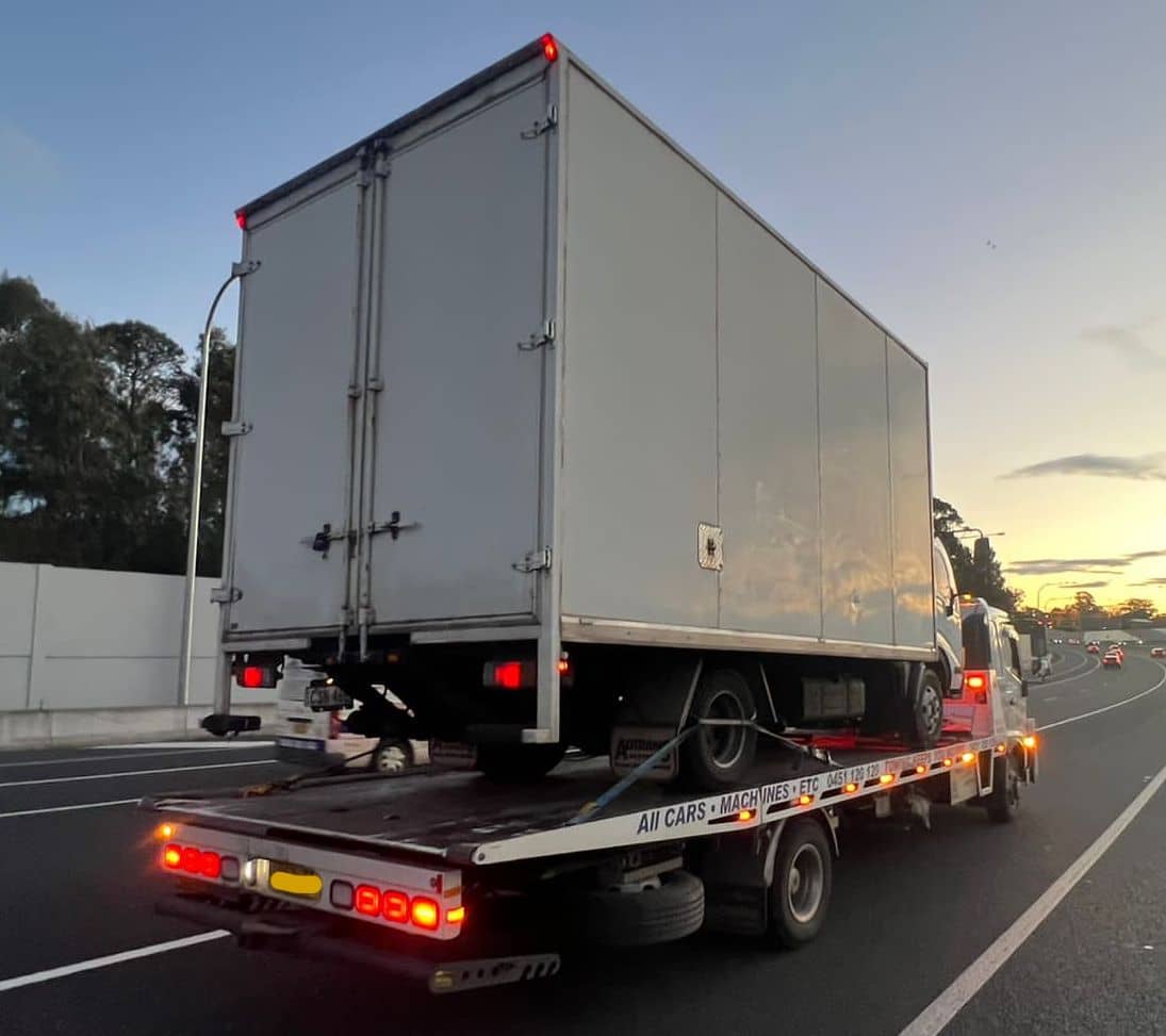 A tilt tray truck towing a small truck.