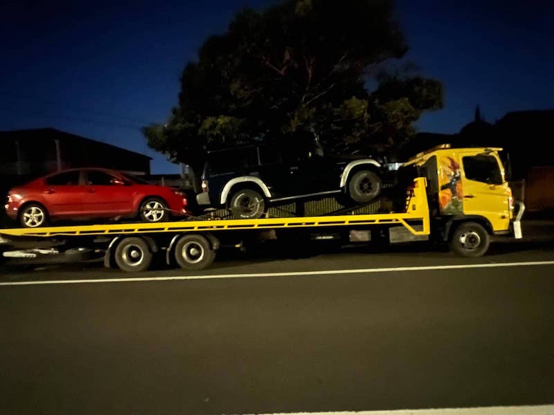 Tow cars on a long tilt tray truck late at night.