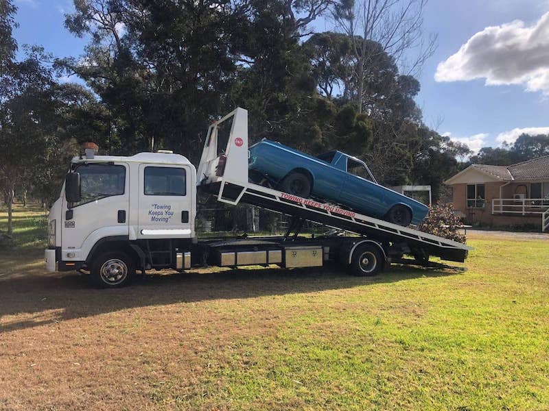 A duel cab tilt-tray towing a classic Australian ute from a farm.