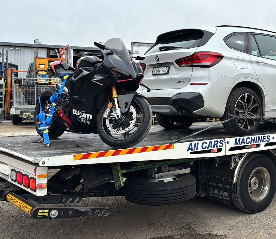 A motorbike and a car being towed on the back of a tow truck.