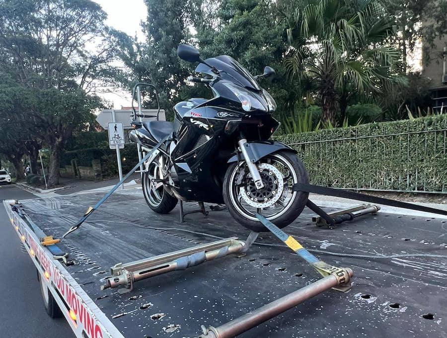 A motorbike on the back of a tilt tray truck tied down.