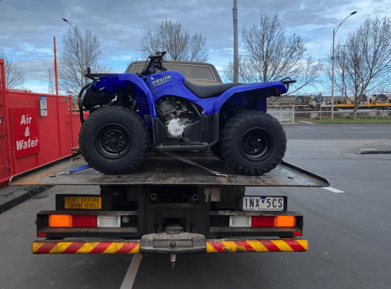 A quad bike and car fitted on the back of a tow truck.