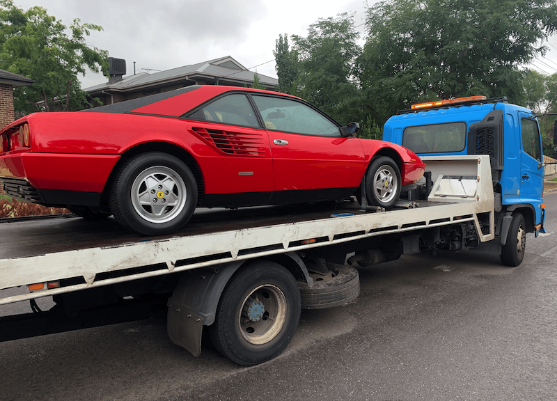 A tilt tray tow truck towing a classic Ferrari.