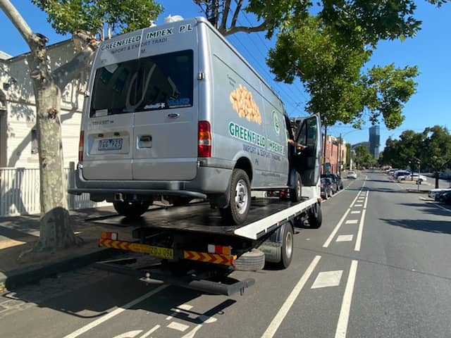 A heavy van is being towed a long distance by a tow truck.